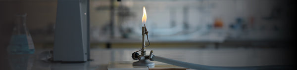 Lab burner with a flame in a laboratory setting, used for flammability testing of materials