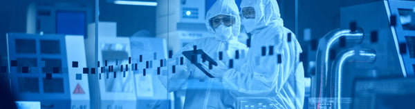 Technicians in cleanroom suits inspecting data on a tablet in a high-tech lab.